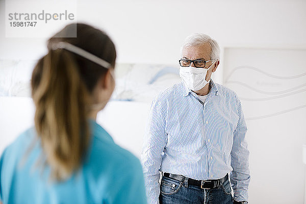 Ein älterer Mann trifft seine weibliche Physiotherapeutin an der Rezeption  die Gesichtsmasken trägt