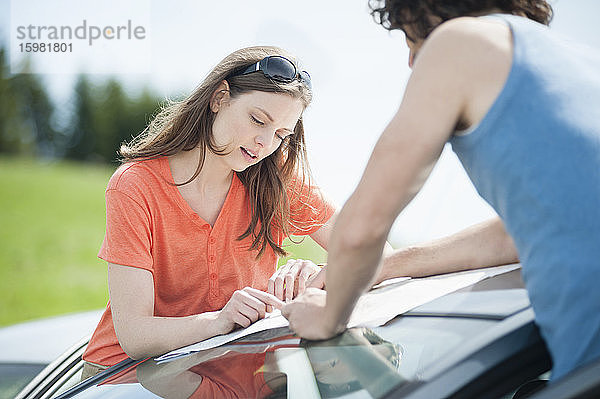 Selbstbewusste schöne Frau  die mit einem Mann auf dem Autodach eine Karte liest  während eines Sommerausflugs