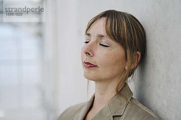 Porträt einer Geschäftsfrau mit geschlossenen Augen  die an einer Betonwand lehnt