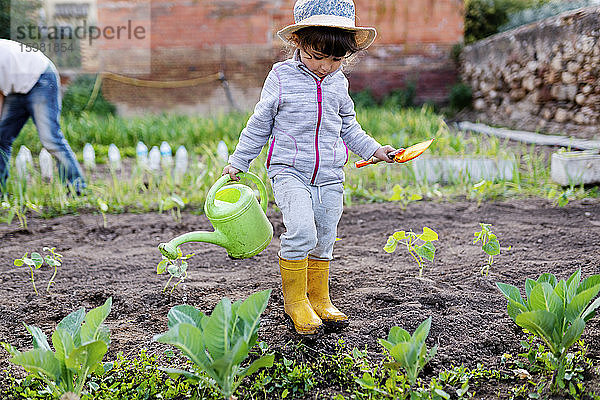 Niedliches Vorschulmädchen mit Schaufel und Gießkanne im Obstgarten in voller Länge