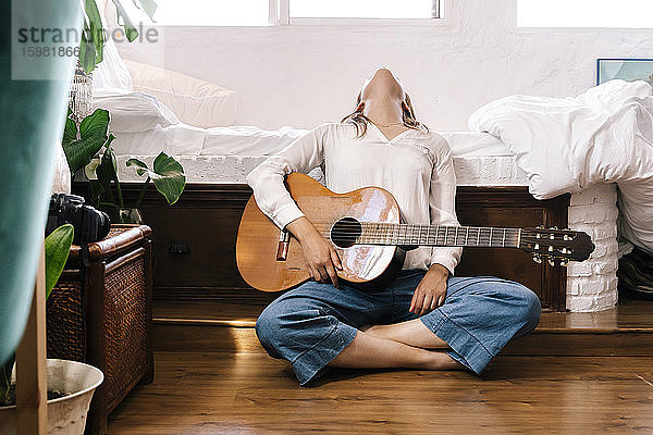 Frau mit Gitarre sitzt auf dem Boden vor dem Bett und lehnt sich zurück