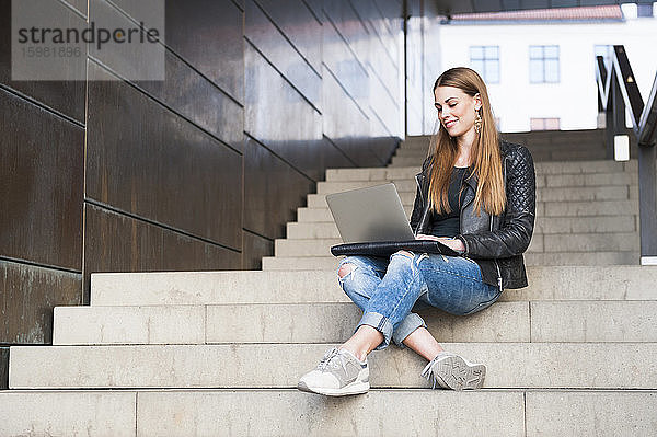 Glückliche junge Frau  die einen Laptop benutzt  während sie auf den Stufen eines unterirdischen Ganges sitzt