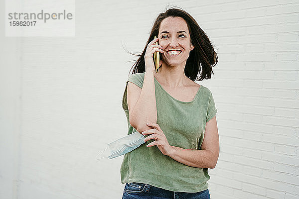 Porträt einer glücklichen Frau am Telefon mit Schutzmaske