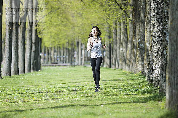 Selbstbewusste junge Frau schaut weg  während sie auf einer Wiese im Park läuft