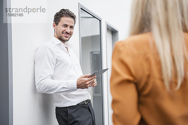 Selbstbewusster Geschäftsmann  der ein digitales Tablet hält und eine Kollegin im Büro ansieht