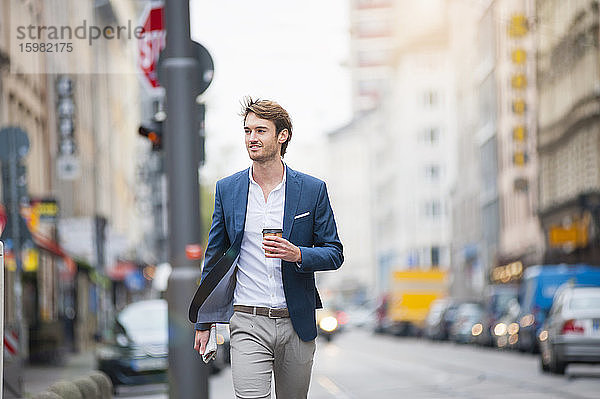 Porträt eines jungen Geschäftsmannes mit Zeitung und Kaffee zum Spazierengehen auf der Straße