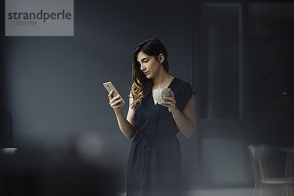 Porträt einer ernsten jungen Frau mit einer Tasse Tee in einem Loft  die auf ihr Handy schaut
