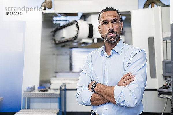 Porträt eines selbstbewussten Geschäftsmannes an einer Maschine in einer Fabrikhalle