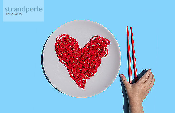 Hand eines kleinen Mädchens  das nach Stäbchen greift  um rot gefärbte herzförmige Spaghetti zu essen