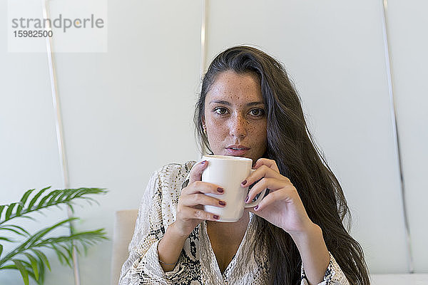 Porträt einer jungen Frau mit Sommersprossen  die zu Hause Kaffee trinkt