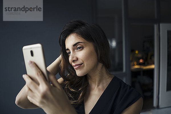 Porträt einer lächelnden jungen Frau  die ein Selfie mit ihrem Smartphone macht
