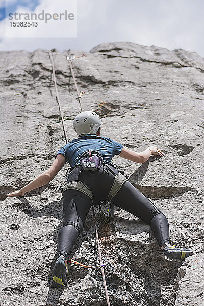 Junge Frau klettert mit Seil an einem sonnigen Tag auf einen Felsen