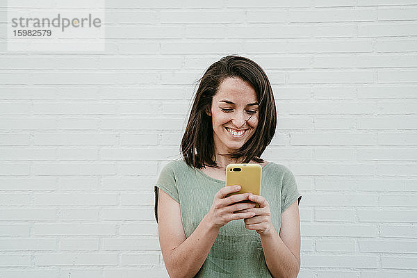 Porträt einer glücklichen Frau  die auf ihr Mobiltelefon schaut