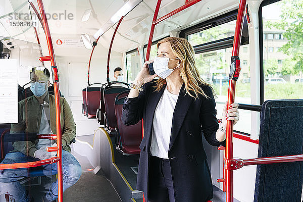 Geschäftsfrau am Telefon mit Schutzmaske in einem öffentlichen Bus  Spanien