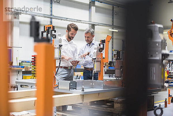 Zwei Männer teilen sich ein Tablet in einer Fabrikhalle