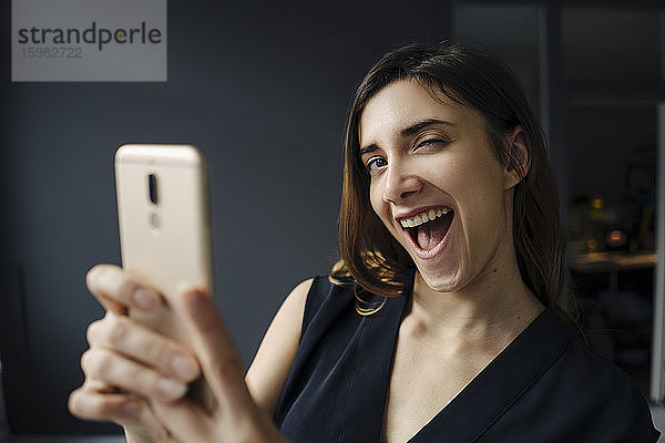 Porträt einer jungen Frau mit Smartphone  die lustige Gesichter zieht