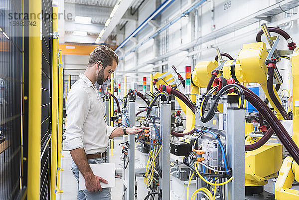 Junger männlicher Ingenieur betrachtet den Roboterarm einer Maschine in einer automatisierten Fabrik