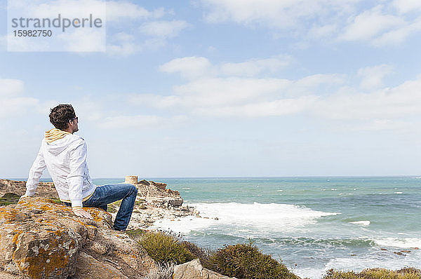 Mann entspannt sich auf einem Felsen an der Küste und schaut aufs Meer  Sardinien  Italien