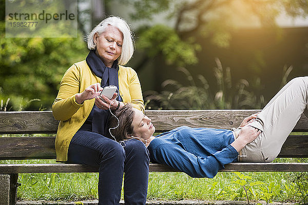 Ältere Frau und erwachsene Tochter entspannen zusammen auf einer Parkbank