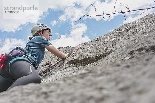 Junge Frau beim Klettern mit Blick auf Felsen gegen den Himmel