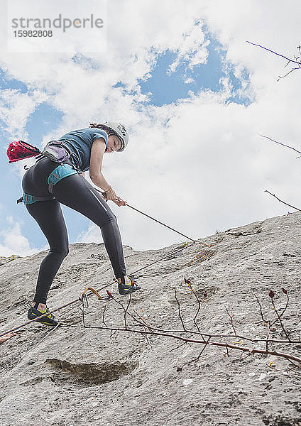 Junge Frau  die sich mit einem Seil an einem Felsen gegen den Himmel abseilt