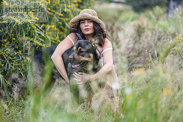 Porträt einer schönen jungen Frau mit Hut  die einen Hund auf Pflanzen umarmt  Alicante  Provinz Alicante  Spanien