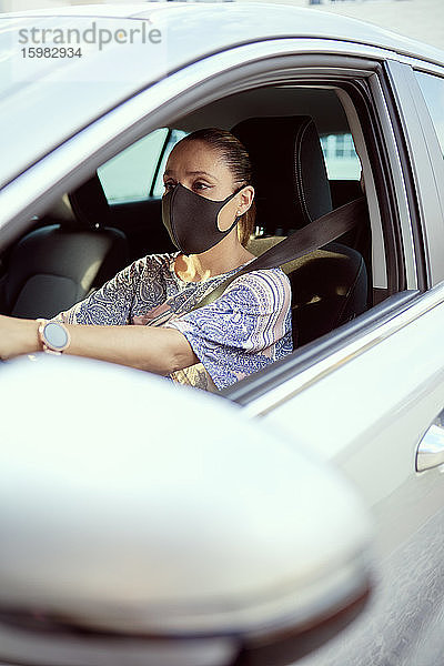 Frau mit Gesichtsmaske beim Autofahren