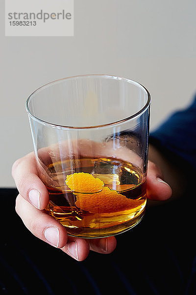 Mann hält Whisky mit Orangenschale