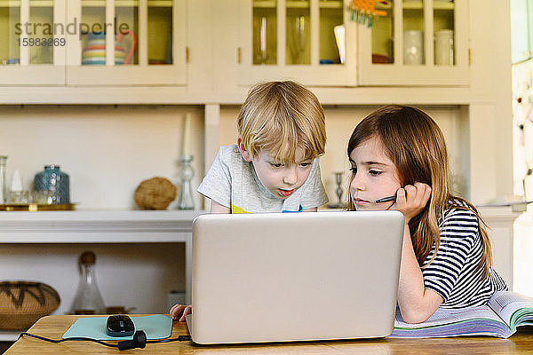 Junge (4-5) und Mädchen (6-7) schauen sich zu Hause einen Laptop an