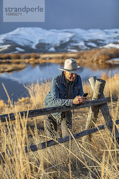 USA  Idaho  Sun Valley  Älterer Mann mit Cowboyhut  der sich an Zauntexte lehnt