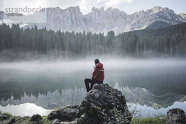Schweiz  Junger Mann sitzt im Morgengrauen am Lago di Carezza in den Dolomiten