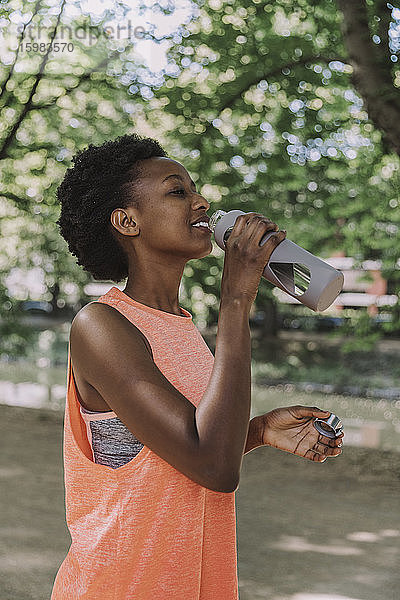 Sportliche junge Frau trinkt Wasser aus einer Flasche