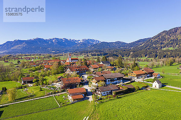 Deutschland  Bayern  Wackersberg  Drohnenansicht einer ländlichen Stadt im Frühling mit Brauneck und Benediktenwand im Hintergrund