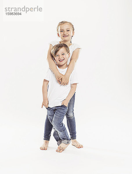 Porträt eines lächelnden Mädchens und ihres jüngeren Bruders vor einem weißen Hintergrund