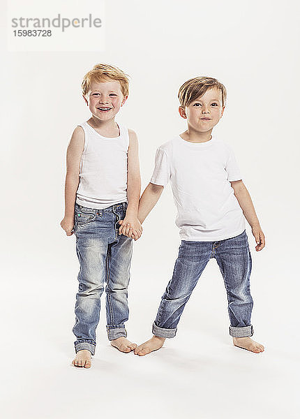 Porträt von zwei kleinen Jungen  die sich vor einem weißen Hintergrund an den Händen halten