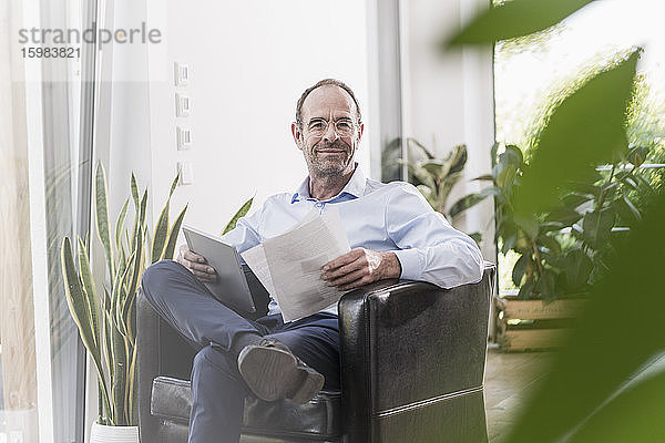 Porträt eines lächelnden Geschäftsmannes mit digitalem Tablet und Dokumenten bei der Arbeit zu Hause