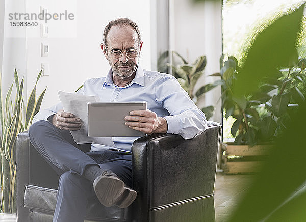 Porträt eines lächelnden Geschäftsmannes mit digitalem Tablet und Dokumenten bei der Arbeit zu Hause