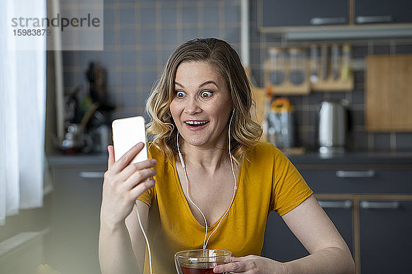 Überrascht Frau mit einem Video-Chat mit Smartphone in der Küche zu Hause