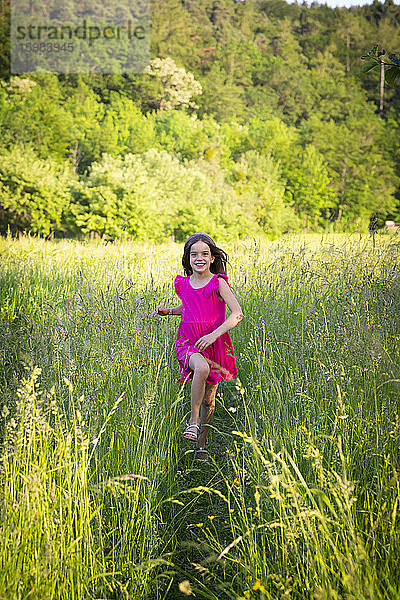 Porträt eines kleinen Mädchens  das lächelnd über eine ländliche Wiese auf die Kamera zuläuft