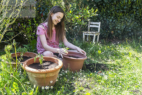 Lächelndes Mädchen beim Eintopfen von Tomatenpflanzen in einem Garten