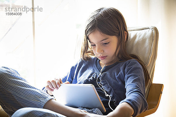 Mädchen sieht sich ein Online-Video an  während sie zu Hause auf einem Sessel am Fenster sitzt