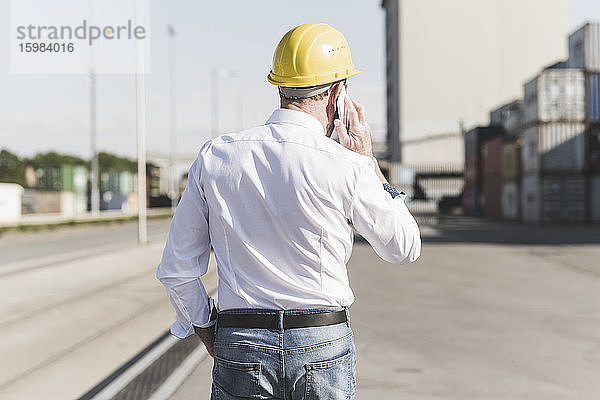 Rückansicht eines telefonierenden Geschäftsmannes mit Schutzhelm auf einem Industriegelände