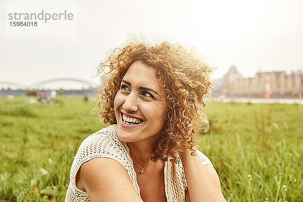 Porträt einer lächelnden Frau  die auf einer Wiese sitzt und zur Seite schaut