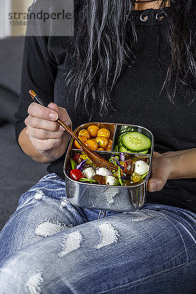 Mittelteil einer sitzenden Frau  die aus einer Lunchbox isst