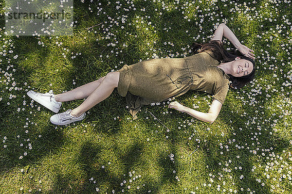 Frau genießt ihre Freizeit  während sie im Gras mit Gänseblümchen liegt