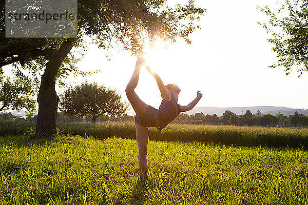 Teenager-Mädchen beim Yoga auf einem grasbewachsenen Feld bei Sonnenuntergang