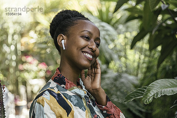 Glückliche junge Frau hört Musik mit Kopfhörern im Garten