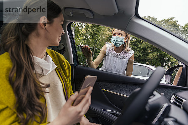 Frau mit Schutzmaske spricht durch ein Autofenster mit einer Frau ohne Maske