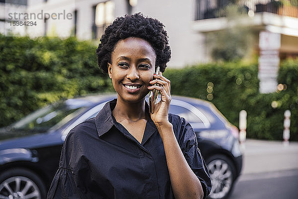 Porträt einer lächelnden jungen Frau beim Telefonieren im Freien