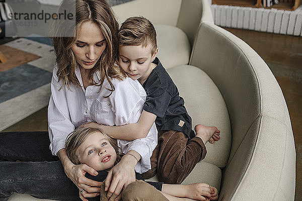 Blonde Frau sitzt mit ihren Söhnen auf dem Sofa im heimischen Wohnzimmer